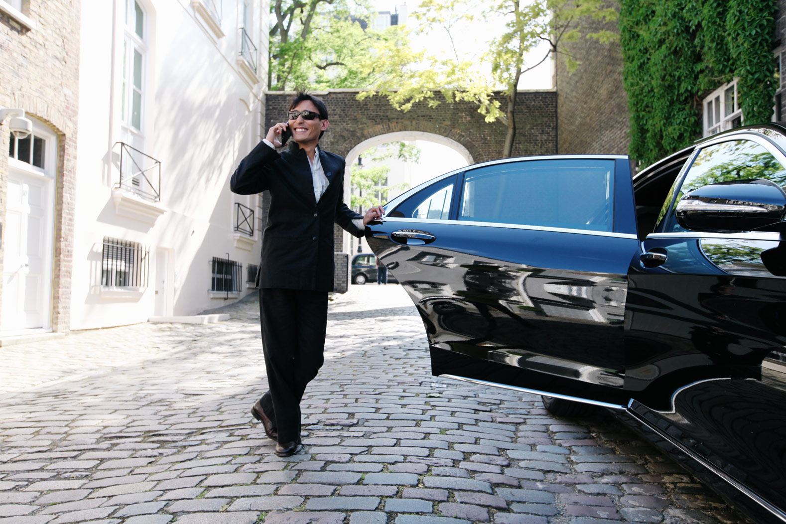 Business man on phone smiling besides black chauffeur car with door open