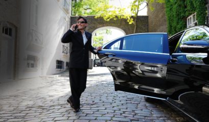Business man smiling and talking on mobile phone beside Mercedes S-Class with rear door open