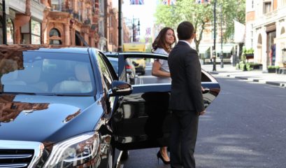 iChauffeur Chauffeur opening door of Mercedes S-Class in London street for smiling passenger