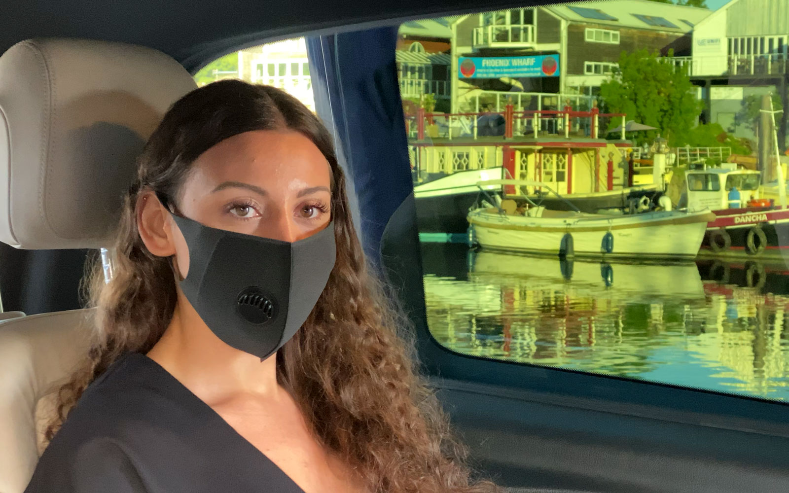 Client in mask in rear of chauffeur driven Mercedes-Benz by the Thames, London