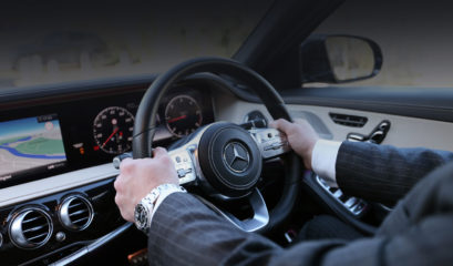 S-Class Mercedes-Benz chauffeur in smart suit, with hands on the steering wheel