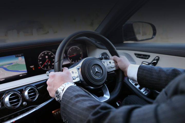 S-Class Mercedes-Benz chauffeur in smart suit, with hands on the steering wheel