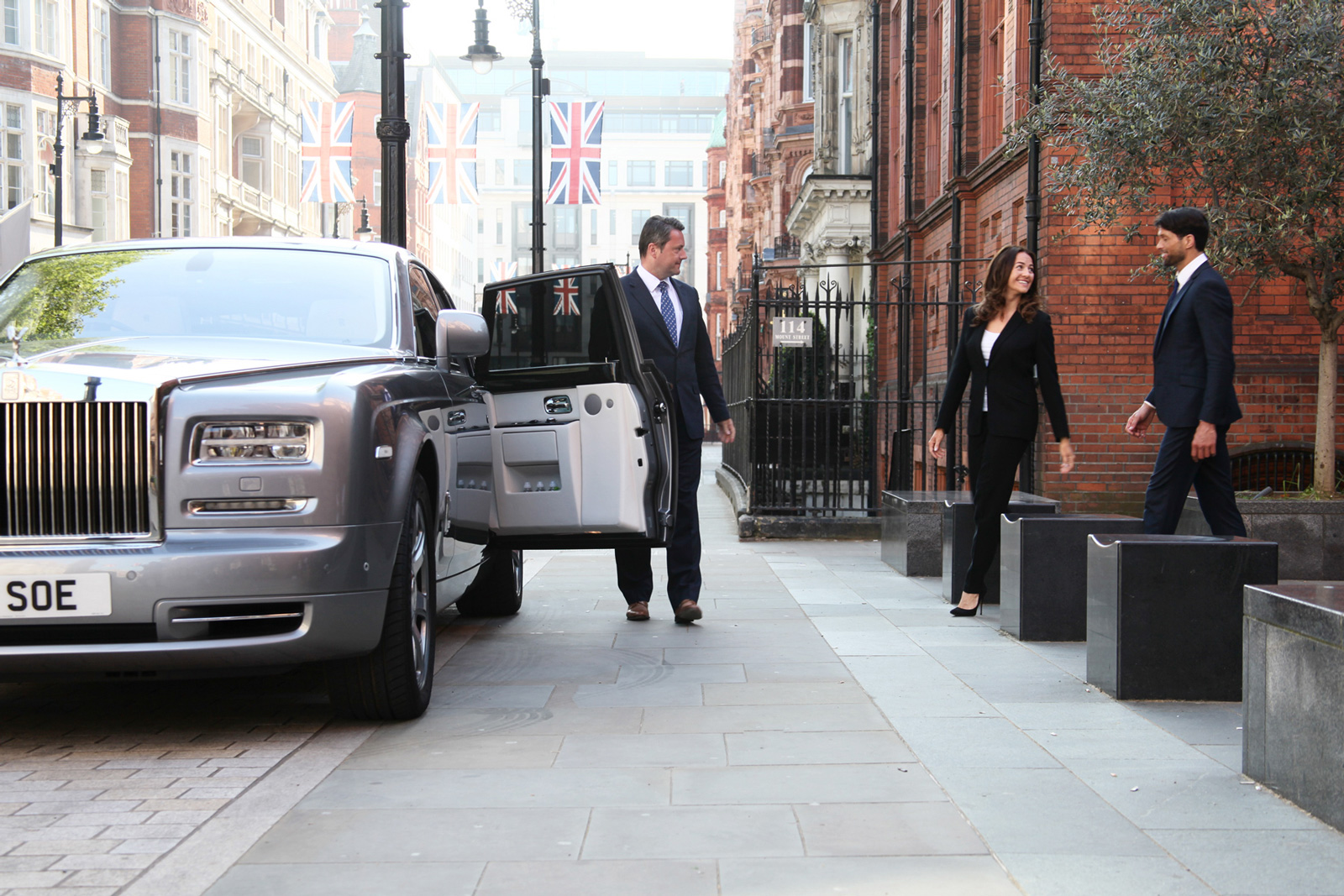 Chauffeur holds door open of Rolls-Royce Phantom as couple approach in London street