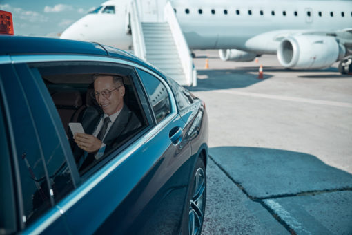 man in chauffeur car next to private plane