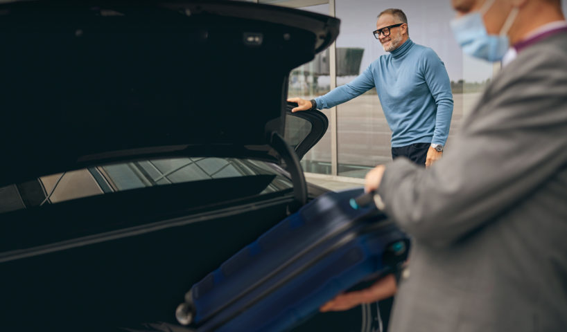 Airport chauffeur loading boot with luggage while happy passenger smiles