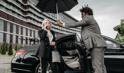 Chauffeur holds umbrella over passenger in front of Mercedes