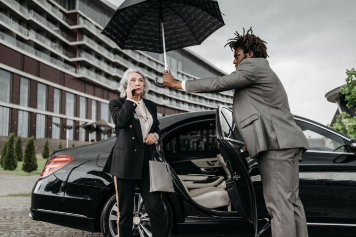 Chauffeur holds umbrella over passenger in front of Mercedes