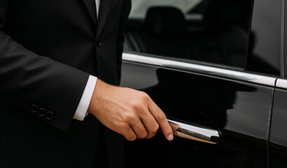 Suited chauffeur opening black car door