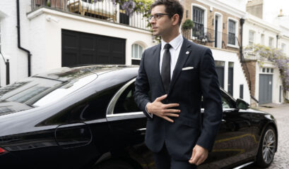 A suited chauffeur standing in front of black Mercedes-Benz S-Class