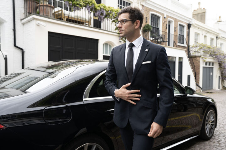 A suited chauffeur standing in front of black Mercedes-Benz S-Class