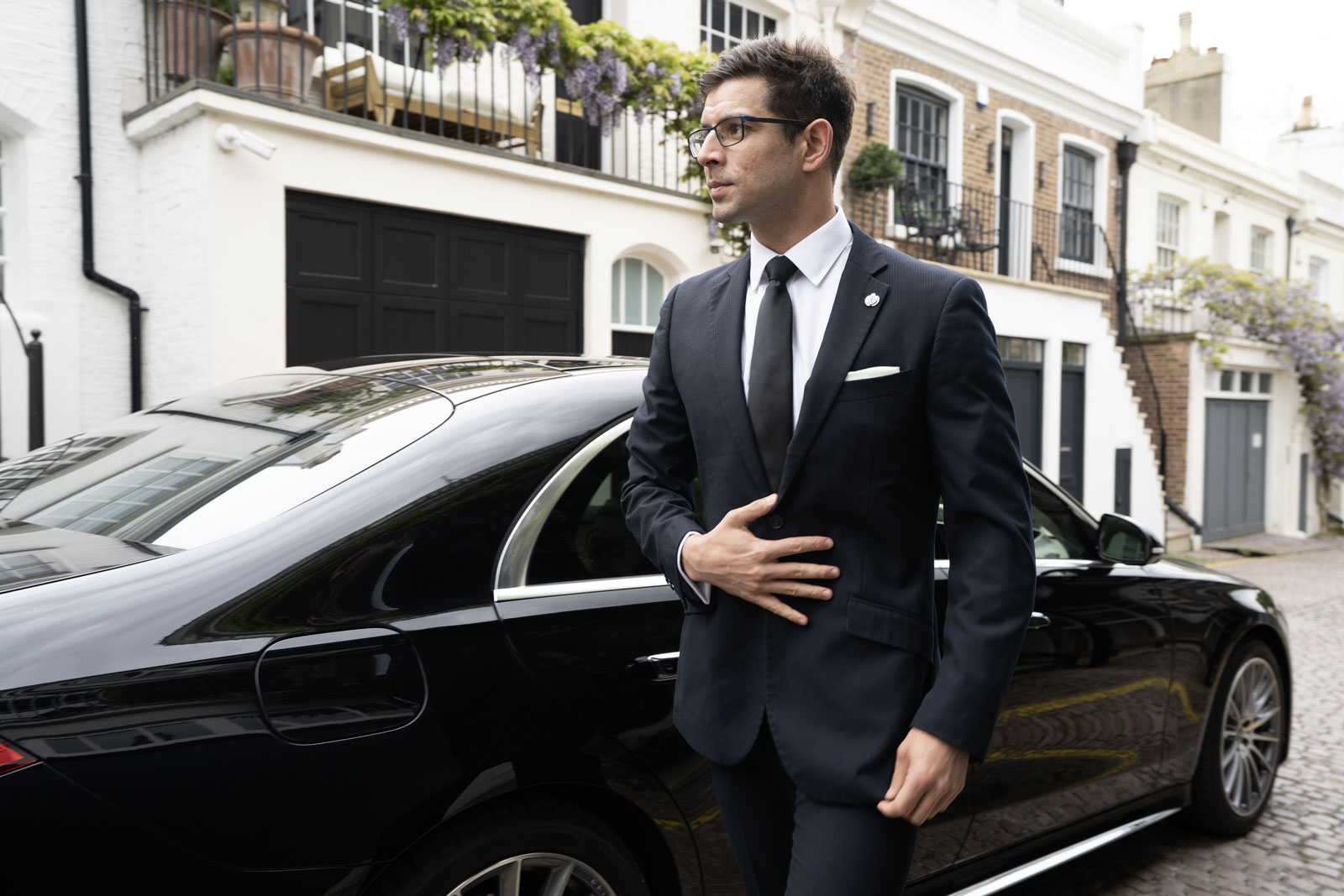 A suited chauffeur standing in front of black Mercedes-Benz S-Class